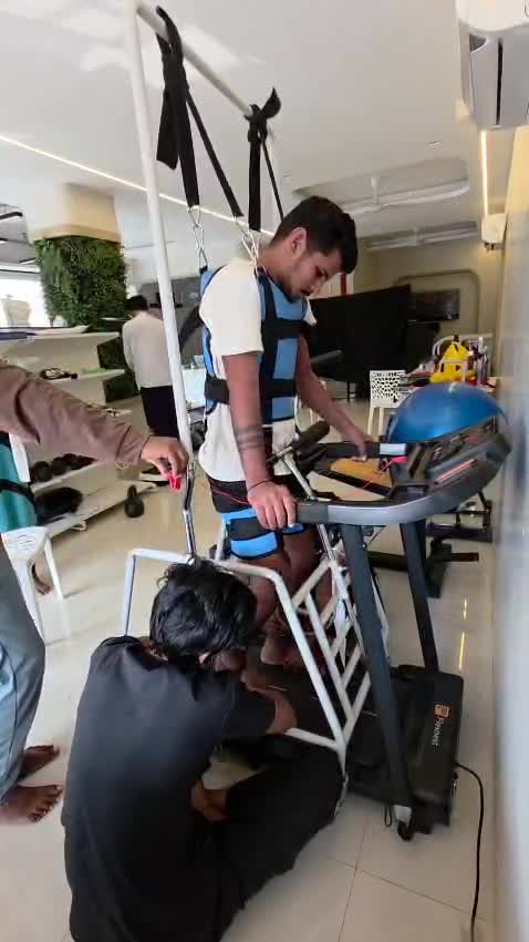 Patient undergoing body-weight supported treadmill gait therapy with therapist assistance